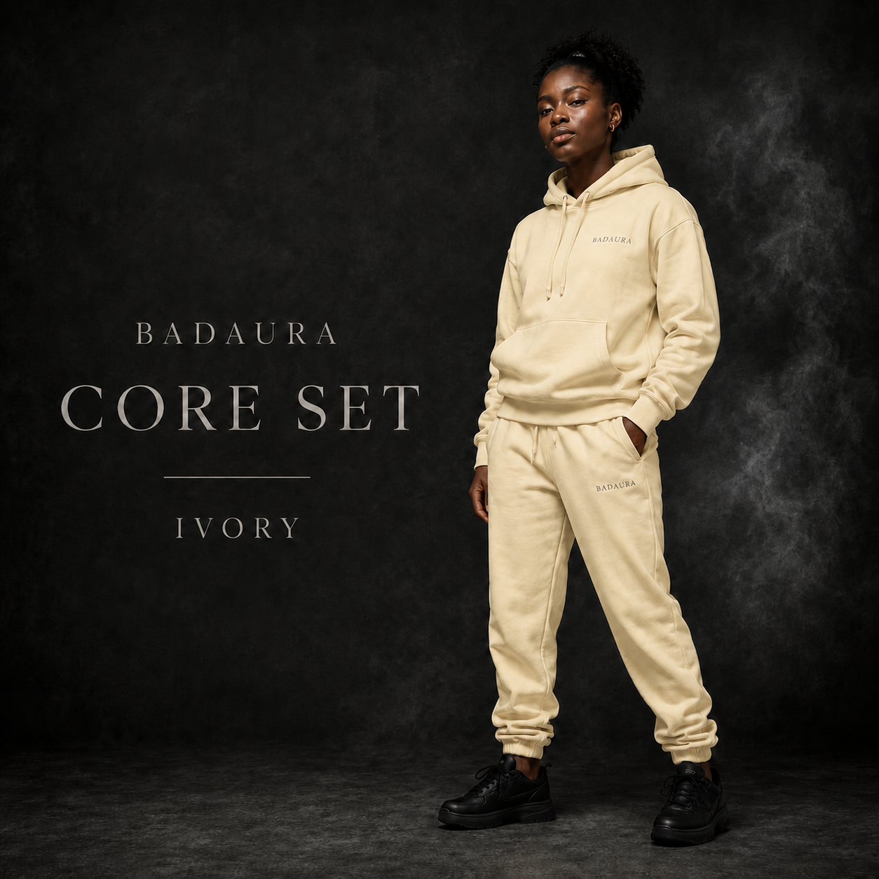 Person wearing a beige hoodie and pants set with 'Badaura' branding on a dark background.